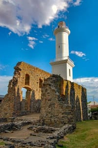 Faro de Colonia del Sacramento, Uruguay, rodeado de ruinas históricas y cielo despejado. Signature DMC en Sudamérica.